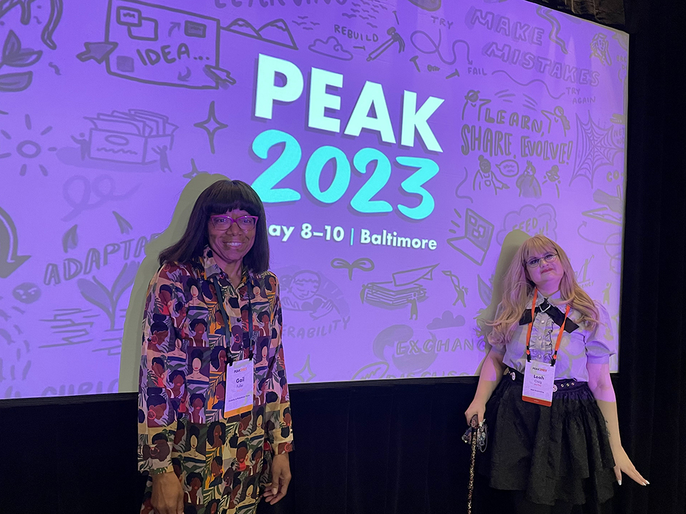 Gail Fuller and Leah Craig standing in front of a screen displaying a purple PEAK2023 slide. The conference took place May 8 - 10 in Baltimore.