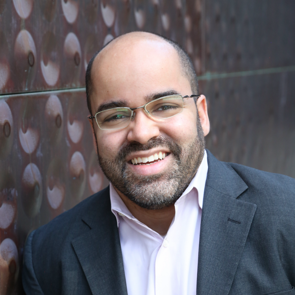 Ryan Easterly, a Black man wearing glasses, a gray jacket, and light colored button down.