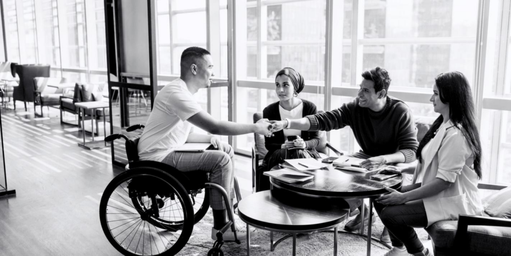 A black-and-white photo of a man in a wheelchair shaking hands with other nonprofit professionals.