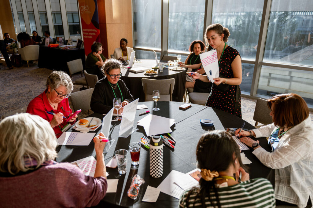 Participants sit around a table writing alt text for images by hand as part of an accessibility activity.