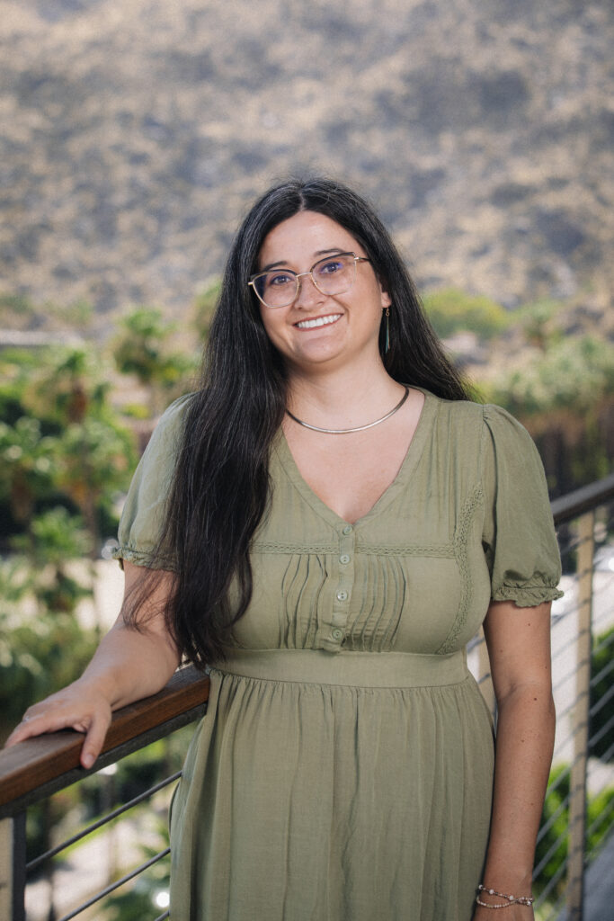 Sofia is standing on a balcony and behind her are palm trees and mountains.